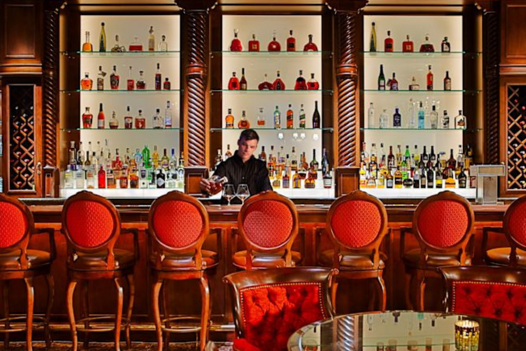 Bartending pouring drinks at a bar with red chairs