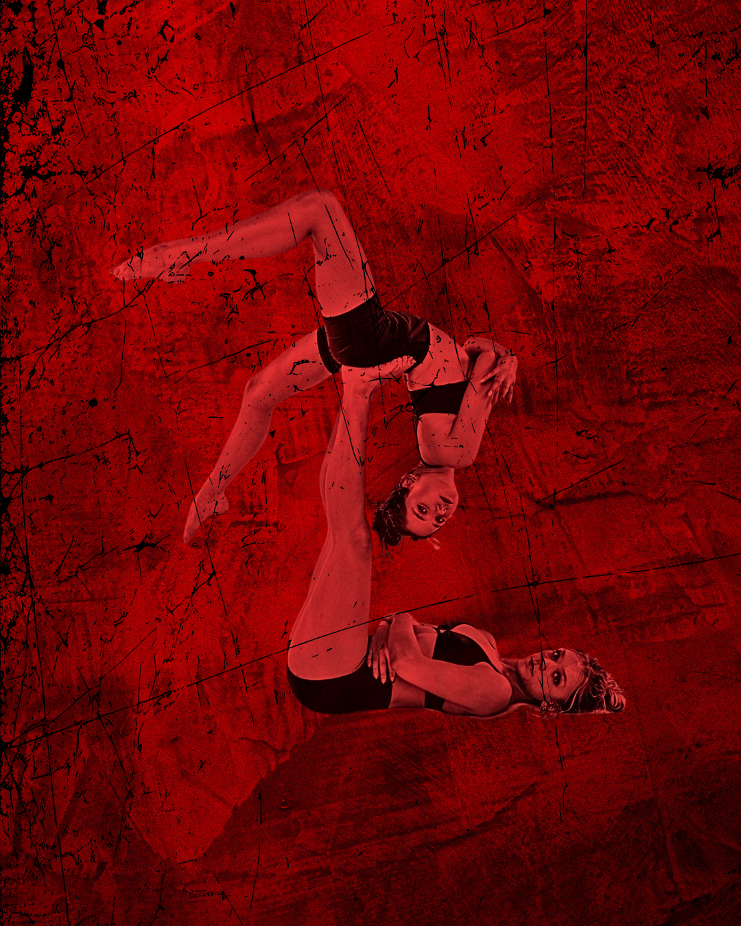 Female dancer lying down with legs lifted while a second female dancer balances on her feet with red lighting and red background