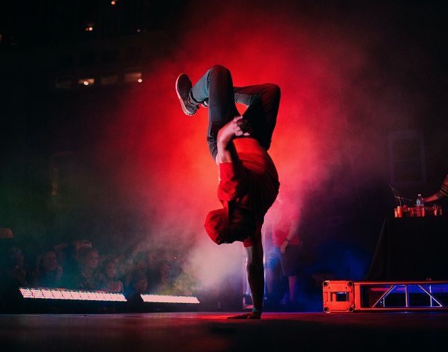 dancer in one-handed hand stand with smoke in the background